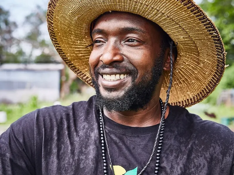 Heru Lewis in front of an agriculture field wearing a straw hat