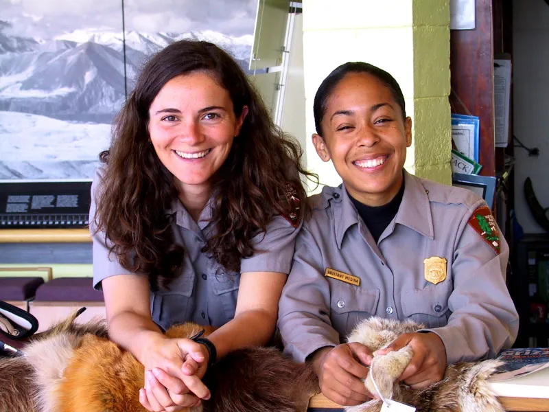 Two National Park Service employees smile while sitting at a desk