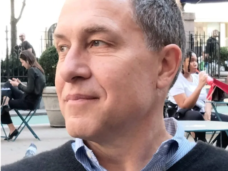 Ted Heisel sits at a cafe outside on a street with others in the background