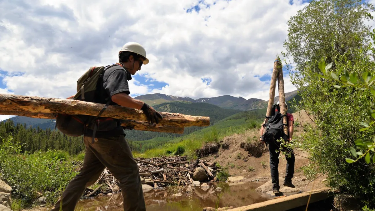young people in hardhats carry cut logs over a mountain trail in Colorado