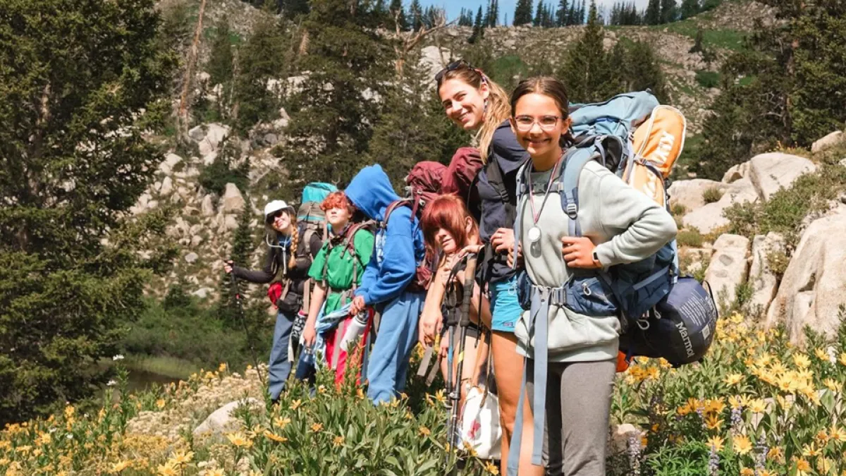 Girl and Her Backpack - a group of girls stands in a row on a trail in the backcountry