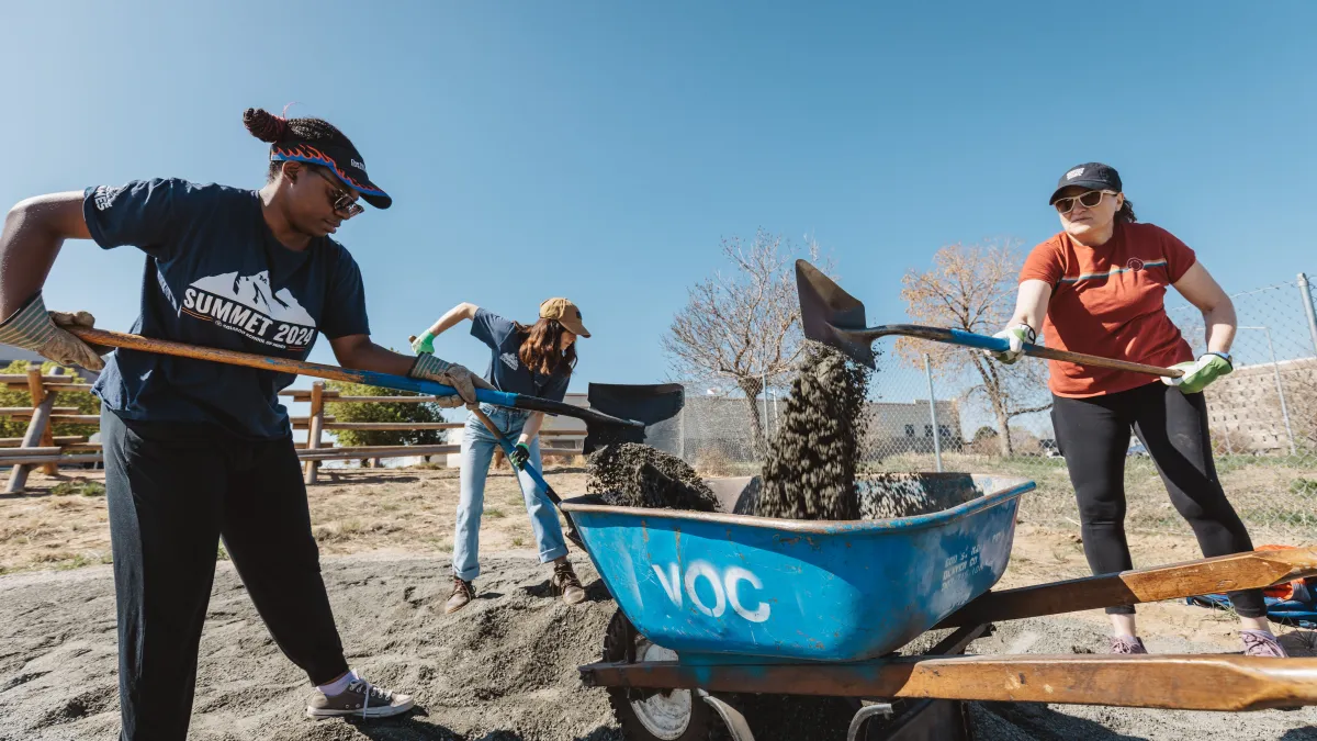 3 people shoveling gravel on a sunny day.