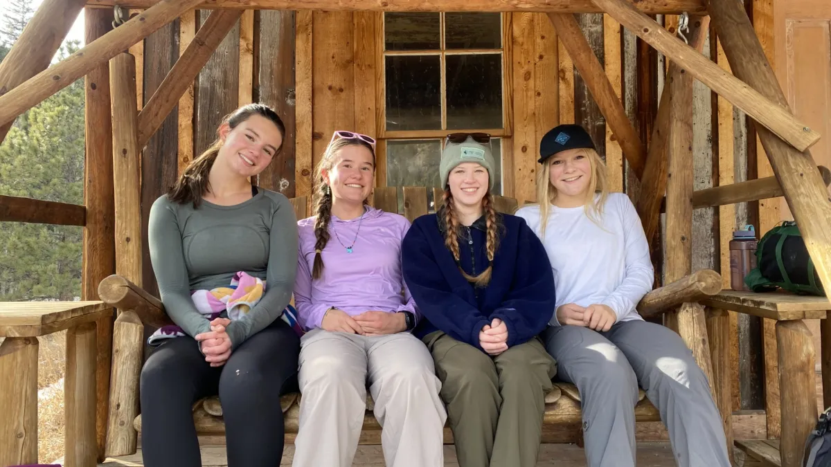 4 Teen Interns sitting on a porch swing outside of a cabin