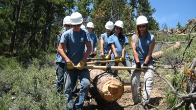 Several youth corps members work together to remove a large log from a trail