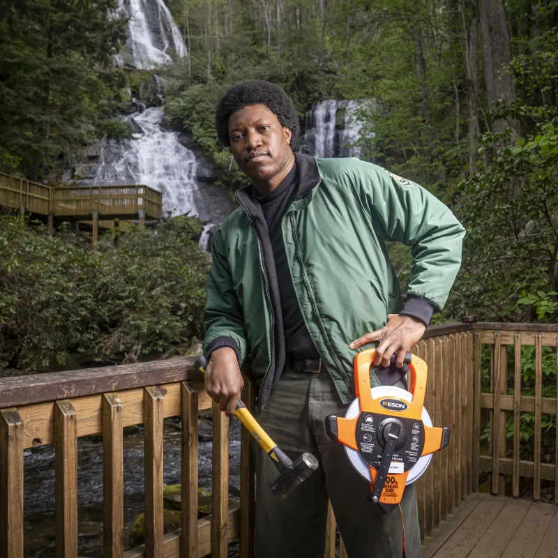 A forest engineer stands on a wooden platform with a hammer and measuring tape
